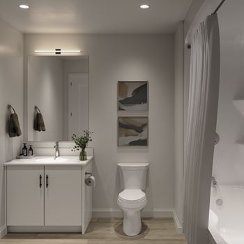 A white bathroom with a toilet, sink, and a painting on the wall at Roxy Apartments, Hamilton, ON